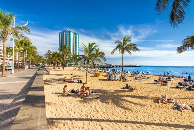 Playa del Reducto beach Arrecife Lanzarote — sandy urban beach with palm trees and blue umbrellas with Gran Hotel in the background
