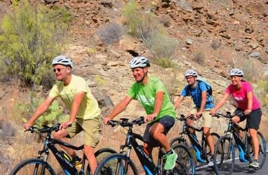 E-bike tour through La Geria vineyards Lanzarote — cyclists riding between volcanic craters and traditional wine estates under blue skies