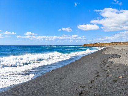 Playa del Janubio Lanzarote — wild cove of black volcanic sand with reddish volcanic cliffs and turquoise Atlantic water on the southwest coast near the Janubio salt flats