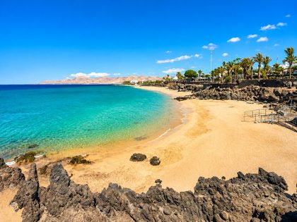 Playa Grande Puerto del Carmen Lanzarote — sheltered urban beach of fine golden sand in a curved bay with turquoise water, palm-lined promenade and the Avenida de las Playas behind