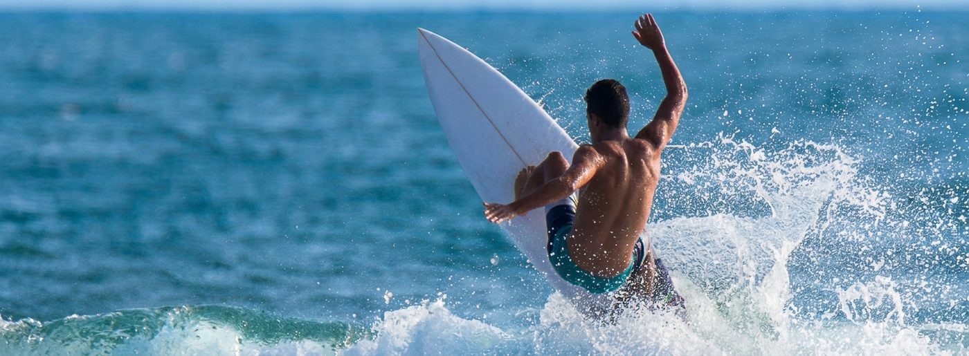 Surfer riding Atlantic wave at Famara beach Lanzarote with dramatic cliffs and turquoise ocean under blue sky